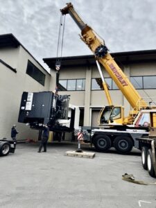 Crane lifting large industrial equipment outside a manufacturing facility